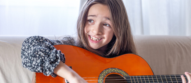 The girl plays the guitar at home. Girl and guitar. High quality photo. The girl plays the guitar and sings songs. Close-up. Playing a stringed instrument.